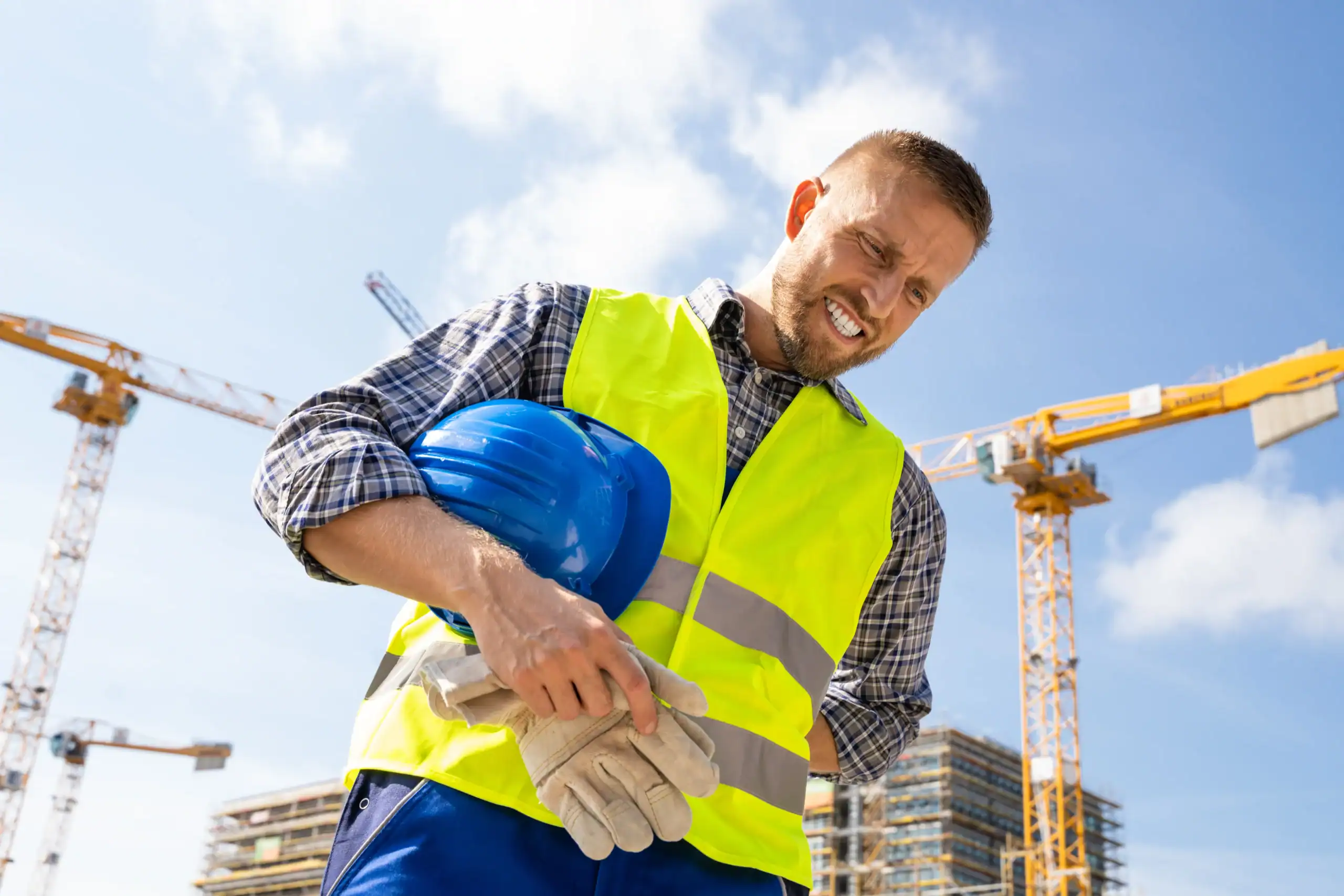 Construction worker smiling with helmet and safety vest at a building site.